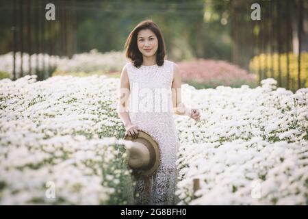 Schöne asiatische Frau zu Fuß und lächeln in tropischen Blumengarten mit Glück Art und Weise mit warmem Sonnenlicht aus dem Hintergrund. Stockfoto