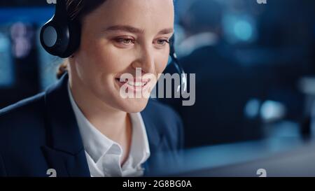 Nahaufnahme Porträt eines glücklichen, schönen technischen Kundendienstspezialisten, der während der Arbeit an einem Computer in einer dunklen Überwachung mit einem Headset spricht Stockfoto