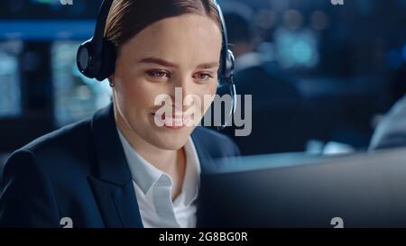 Nahaufnahme Porträt eines glücklichen, schönen technischen Kundendienstspezialisten, der während der Arbeit an einem Computer in einer dunklen Überwachung mit einem Headset spricht Stockfoto