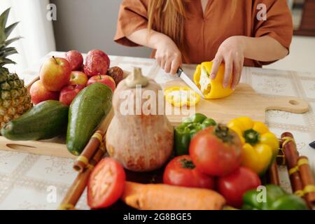 Nahaufnahme einer jungen Frau, die am Küchentisch sitzt und gelben Paprika schneidet Stockfoto