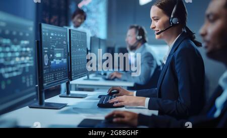 Happy Beautiful Technical Customer Support Specialist Einen Headset-Anruf während der Arbeit an einem Computer in einem dunklen Überwachungs- und Kontrollraum gefüllt Stockfoto