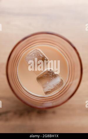 Glas mit Eiskaffee mit Milch und zwei Eiswürfeln auf Holztisch, Draufsicht, flach Stockfoto