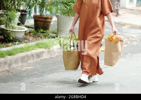 Frau in langen Leinenkleid und Turnschuhen mit schweren Taschen und frischen Lebensmitteln Stockfoto