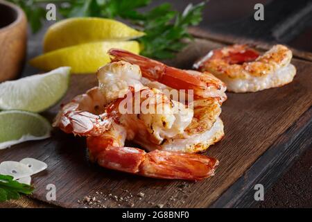 Gegrillte Garnelenschwänze mit Zitrone, Limette, Knoblauch und Gemüse auf Holzbrett Stockfoto