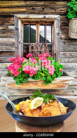 Traditionelles österreichisches Essen (Wiener Schnitzel) gegen traditionelles Häuschen in Kaprun, Österreich Stockfoto