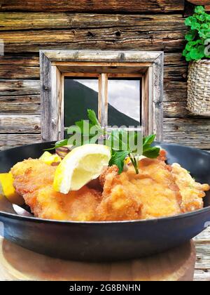 Traditionelles österreichisches Essen (Wiener Schnitzel) gegen traditionelles Häuschen in Kaprun, Österreich Stockfoto