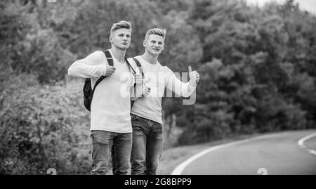 Anhalter und Auto mit Daumen hoch Geste auf dem Land. Unterwegs. Genießen Sie die Sommerwanderung. Auf der Suche nach Transport. Zwillinge zu Fuß entlang der Straße Stockfoto