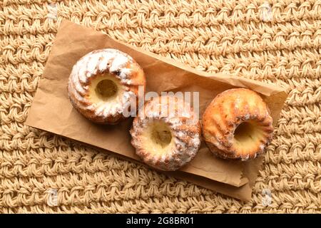 Drei hausgemachte, frisch gebackene Muffins auf braunem Papier, Nahaufnahme, auf einer Strohmatte, Draufsicht. Stockfoto