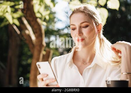 Erfolgreiche junge Geschäftsfrau, die im Café im Freien sitzt und das Smartphone benutzt Stockfoto