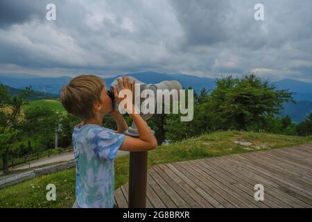 Blondes Kind, das durch das Fernglas auf dem Gipfel blickt und den Blick auf die malerischen Berge genießt Stockfoto