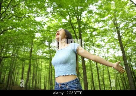 Asiatische aufgeregt Frau feiert Urlaub Strecken Arme und Schreien in einem grünen Wald Stockfoto
