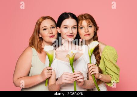 Frau mit Vitiligo hält Calla Lilie in der Nähe von Freunden isoliert auf rosa Stockfoto