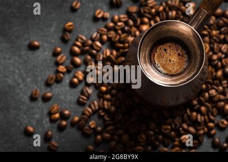 Heißer Kaffee in türkischem (Cezve) und geröstete Kaffeebohnen auf schwarzem Hintergrund. Türkische Kaffeekomposition. Stockfoto