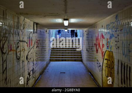 Figuren laufen die Stufen eines schmuddeligen U-Bahn-Tunnels unter einer Eisenbahnlinie hinauf, Wände mit Graffiti bedeckt Stockfoto