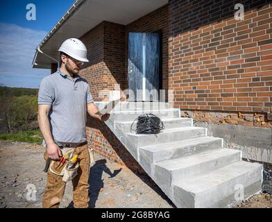 Ein Elektriker hält eine Bauzeichnung in den Händen und inspiziert ein Arbeitsobjekt. Stockfoto