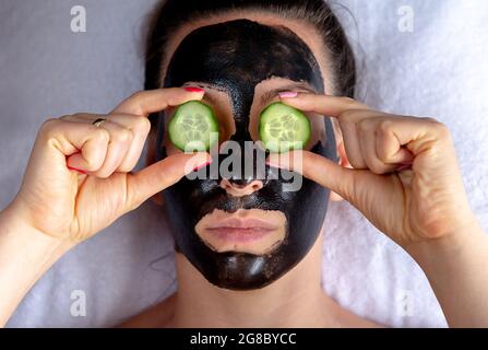 Natürlich aussehendes Mädchen mit schwarzem Caracol Gesichtsmaske auf weißem Handtuch im Spa Salon legen Stockfoto