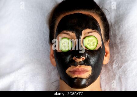 Natürlich aussehendes Mädchen mit schwarzem Caracol Gesichtsmaske auf weißem Handtuch im Spa Salon legen Stockfoto