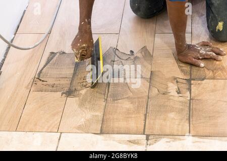 Arbeiter, der die neu verlegte Keramikfliese mit Fugenmaterial bemundet. Bewegungsunschärfe beabsichtigt. Stockfoto