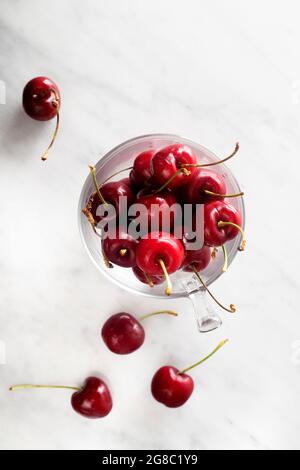 Flacher Glasbecher mit Kirschen auf Marmortisch Stockfoto