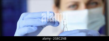 Krankenschwester in Maske und Handschuhe halten Ampulle der Medizin Nahaufnahme Stockfoto