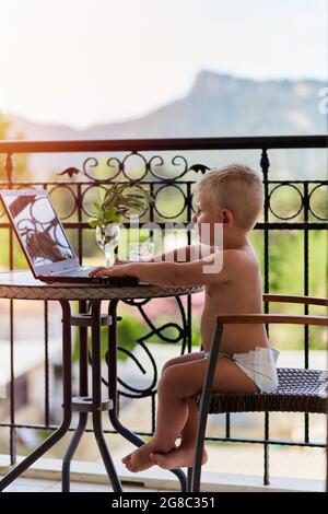 Kaukasischer Kleinkind Junge in Windel spielt auf dem Laptop auf der Terrasse an sonnigen Tag. Neue Generation von Kindern. Spiele spielen, Zeichentrickfilme vor der Maus ansehen Stockfoto