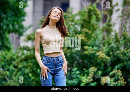 Schlankes Teenager-Mädchen steht im Stadtpark mit geschlossenen Augen. Stockfoto