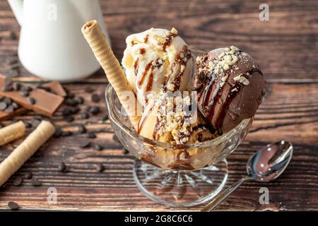 Schokolade, Rahm und Karamell-Roma-Eis in einer Glasschüssel mit Haselnuss- und Schokoladensauce darüber gegossen. Stockfoto