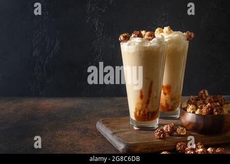 Leckerer Bananenmilchshake garniert mit Karamell, Schlagsahne, Popcorn auf dunklem Grund. Vertikales Format Stockfoto