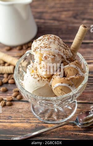 Walnuss-, Creme- und Karamell-Roma-Eis in einer Glasschüssel mit gemahlenem Kaffee und weißer Schokoladensauce darüber gegossen. Stockfoto