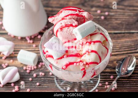 Erdbeer-, Banane- und Rahm-Roma-Eis in einer Glasschüssel mit roter Sauce darüber gegossen. Stockfoto