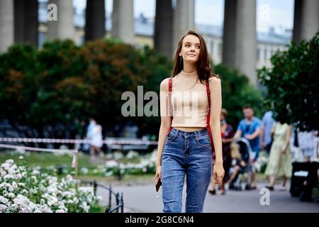 Schlanke junge Frau in Jeans und Tank-Top geht am Sommerabend durch die Stadt. Stockfoto