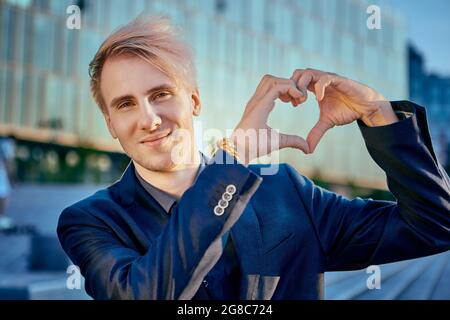 Der junge kaukasische Geschäftsmann zeigt Herz mit seinen Händen. Stockfoto