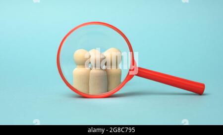 Holzfiguren von Männern und eine rote Lupe auf blauem Hintergrund. Rekrutierung für das Unternehmen, Gleichgesinnte und Teamarbeit. Suchen Sie nach Märchen Stockfoto