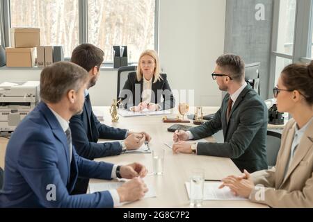 Eine Gruppe von Geschäftsleuten, die am Tisch sitzen und ihrem Vorgesetzten im Zentrum während der Geschäftsbesprechung im Büro zuhören Stockfoto