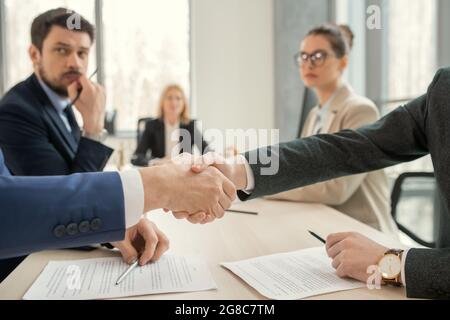 Nahaufnahme von Geschäftsleuten, die sich während einer Besprechung im Büro die Hände schütteln, während sie am Tisch sitzen Stockfoto