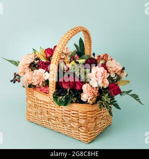 Ein schöner Blumenstrauß in einem gelben Korbkorb steht auf blauem Hintergrund. Leer für eine Grußkarte. Verschiedene Sommerblumen. Stockfoto