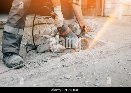 Ein Arbeiter mit einem Schleifer schneidet den Betonpflaster der Straße und Funken fliegen. Bau und Reparatur der Fahrbahn. Stockfoto