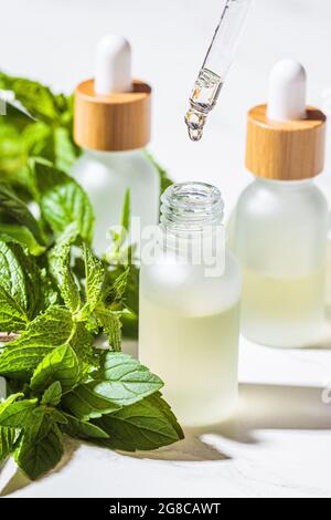 Ätherisches Minzöl in Glasflaschen, weißer Marmorhintergrund, Nahaufnahme. Haut- und Körperpflegekonzept. Stockfoto