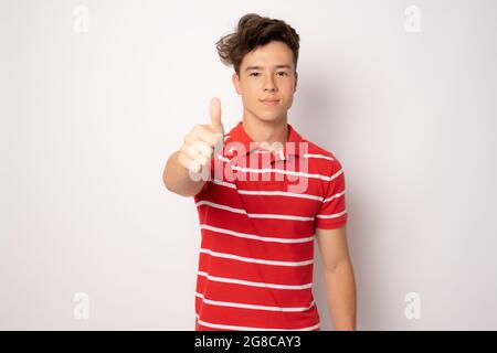Junger Mann im gestreiften Poloshirt mit Daumen nach oben isoliert auf weißem Hintergrund. Stockfoto