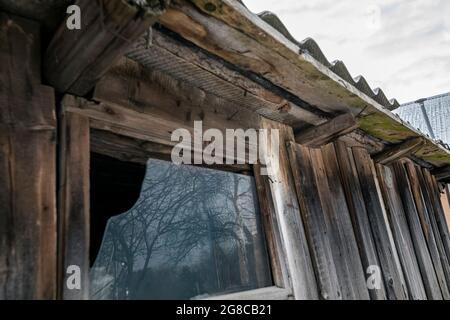 Kaputtes Fenster durch einen alten hölzernen Schuppen. Spiegelung von Bäumen im Fenster. Stockfoto