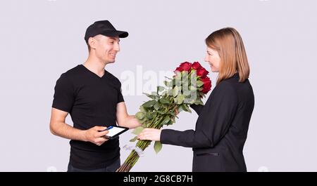 Geschäftsfrau bekam einen Blumenstrauß vom Kurier in schwarzer Uniform und sie muss für die Lieferung unterschreiben. Stockfoto
