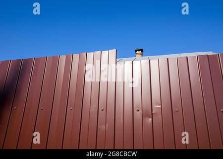 Ein Zaun aus profiliertem Blech gegen einen blauen Himmel. Abstrakte Kunstfotografie. Stockfoto