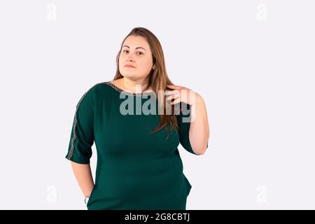Meditative blonde Frau plus Größe in grünem Kleid posiert vor der Kamera und berührt ihre langen Haare, die nach vorne schauen. Stockfoto