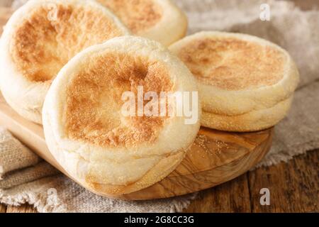 Nur aus dem Ofen Englische Muffin-Brötchen Nahaufnahme auf einem Holzbrett auf dem Tisch. Horizontal Stockfoto