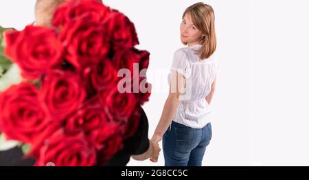 Der Mann will ihrer Freundin anlässlich der Verlobung einen Strauß roter Rosen mit schönem Gesicht schenken. Stockfoto