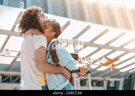 Ein junges internationales Paar trifft sich mit Gepäck am Abflugbereich des Flughafens, umarmt sich glücklich und verabschiedet sich vor dem Urlaub oder einer Geschäftsreise Stockfoto