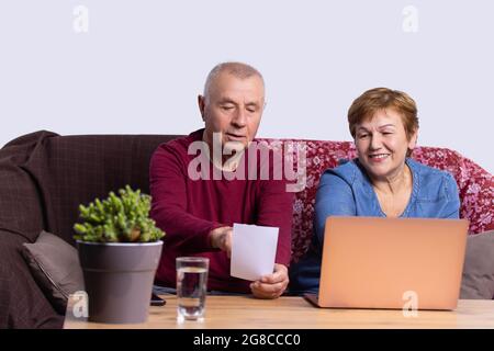 Schönes altes Paar, das auf dem Sofa vor dem Computer sitzt und der Mann zeigt das Bild seiner Frau. Stockfoto