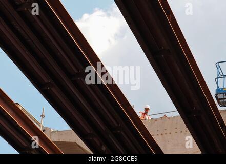 12. Juli 2021, Brandenburg, Potsdam: Ein Arbeiter geht an einem der Segmente der alten Brücke auf der Baustelle der Hochbrücke der Landstraße L40 Nuthestraße entlang. Aufgrund von Platzmangel werden die rund 30 Meter langen und 600 Tonnen schweren Beton- und Betonstahlabschnitte in mehreren Teilschritten auf den Stahlschienen hydraulisch hinter dem Abutment der Friedrich-Engels-Straße gezogen, wo der alte Überbau zerkleinert und abtransportiert wird. Die Sanierung der Hochstraßenbrücke soll im Oktober 2022 abgeschlossen sein. Foto: Soeren Stache Stockfoto