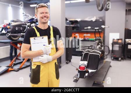 Junger männlicher Schlosser in Uniform steht in der Werkstatt und hält das Klemmbrett mit Dokumenten in den Händen Stockfoto