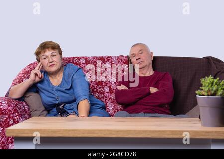 Seniorenpaar zusammen zu Hause Altersheim Konzept Fernsehen sitzen auf der bequemen Couch mit Blumentopf am Tisch. Stockfoto